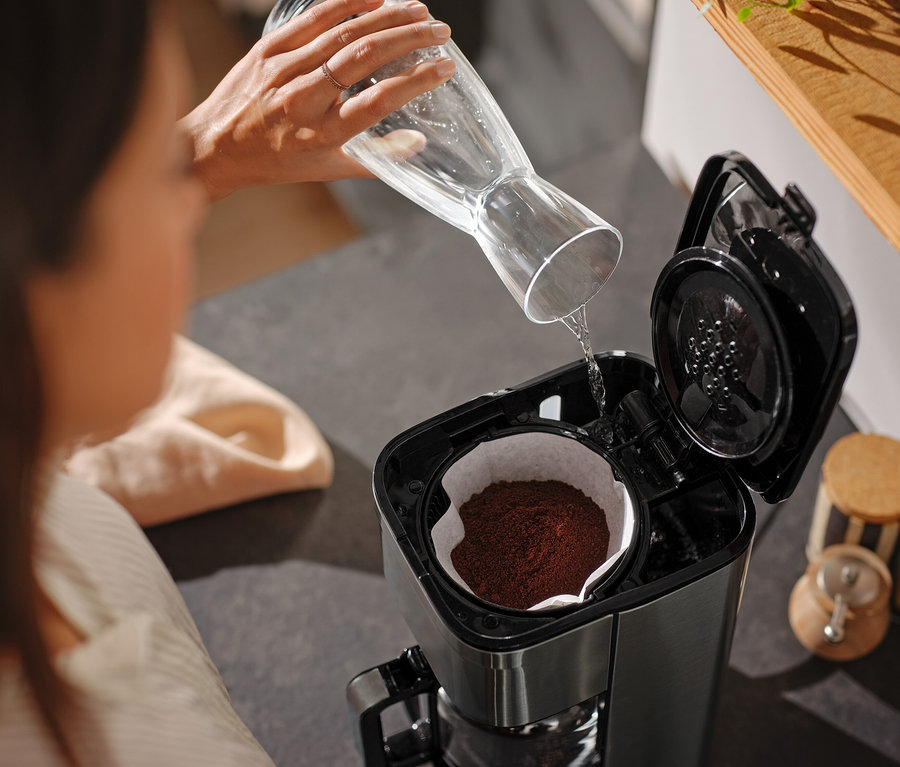 Žena nalévá vodu ze skleněné karafy do kávovaru.