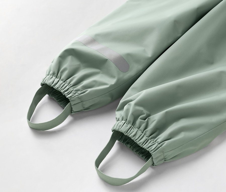 Detailní záběr spodní části světle zelených kalhot s elastickými manžetami a poutky na nohy.