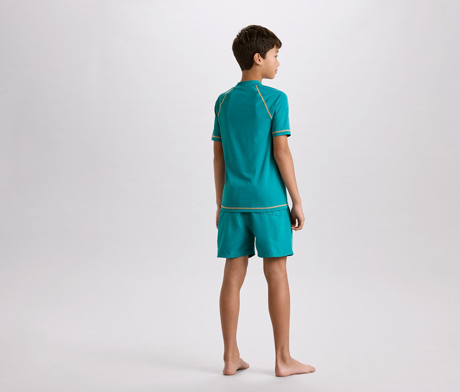 Chlapec zezadu, oblečený v tyrkysovém tričku a šortkách se zlatými ozdobnými švy.