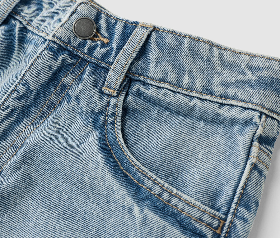 Detail světle modrých džínů s knoflíkem a kapsou.