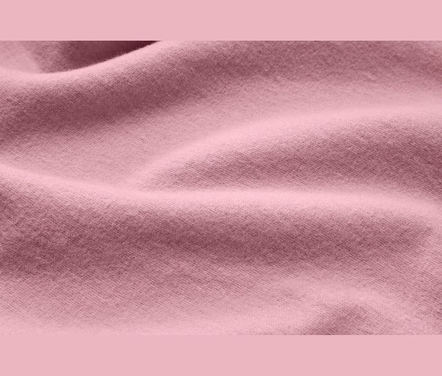 Detail měkké, růžové látky s jemnými záhyby a texturou.
