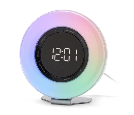 Kulatý budík s digitálním displejem zobrazujícím 12:01 a duhovým podsvícením po obvodu, stojící na stříbrném podstavci.