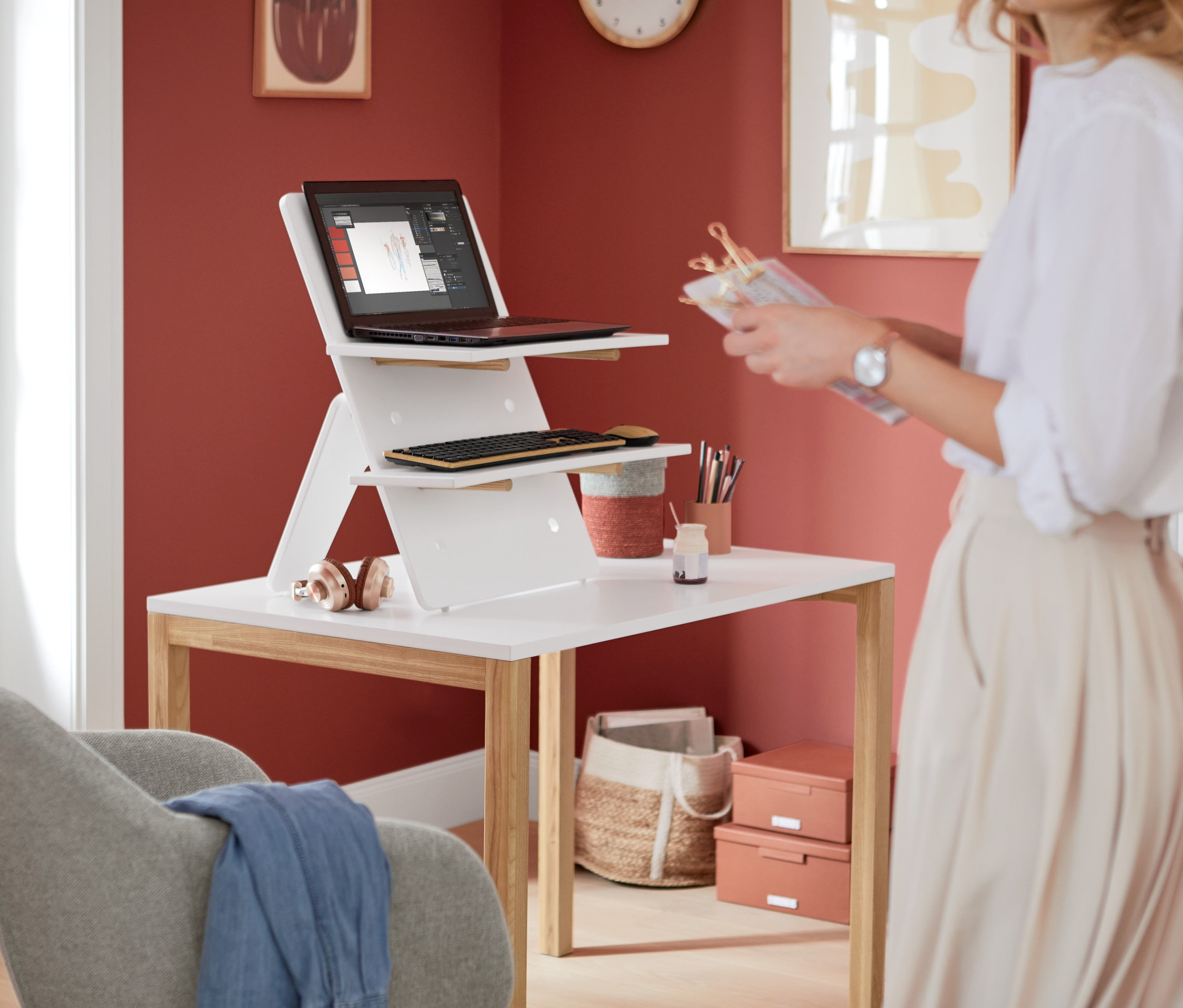 Žena stojí vedle bílého stolu s bílým nástavcem na stůl, na kterém je notebook a klávesnice.