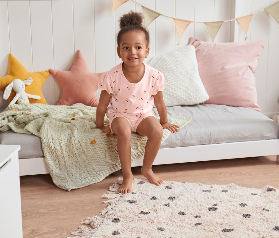 Holčička sedí na posteli v krátkém pyžamu.