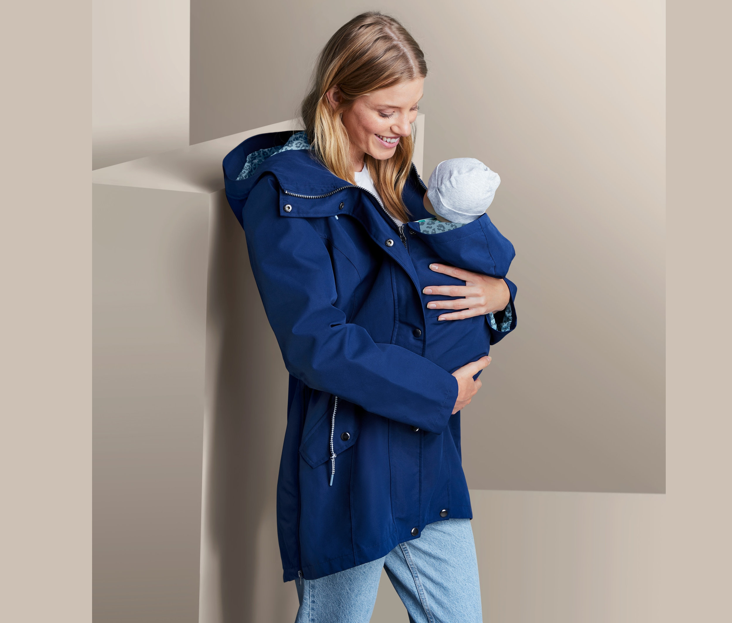 Žena drží dítě v těhotenské bundě do deště.