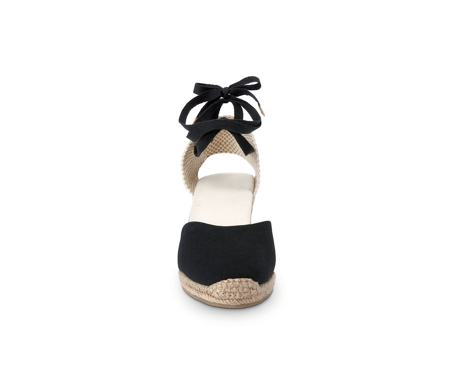 Detail dámské espadrilky s klínovým podpatkem a černou stuhou.