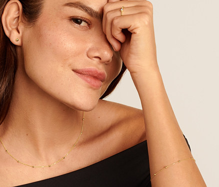 Žena se zlatým prstenem s kuličkami a zirkonem 585, zlatým řetízkem s kuličkami 585, zlatými náušnicemi s kuličkami 585 a zlatým náramkem s kuličkami 585.