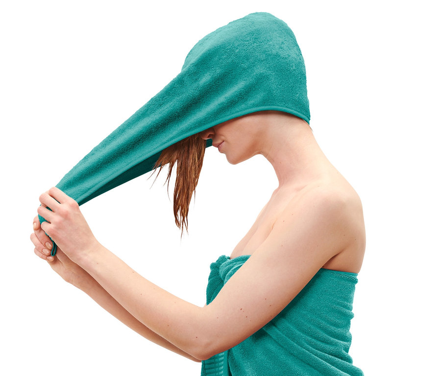 Žena si nasazuje modrozelený ručníkový turban.