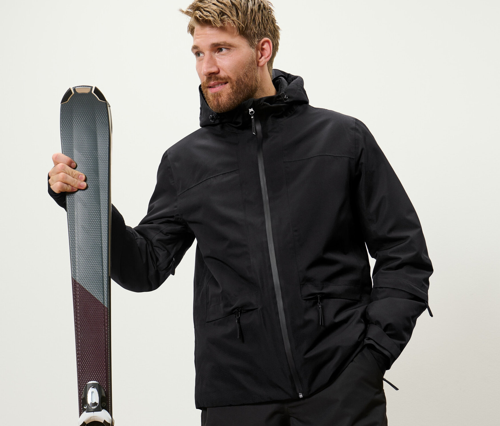 Muž držící lyže. Má na sobě černou lyžařskou bundu.