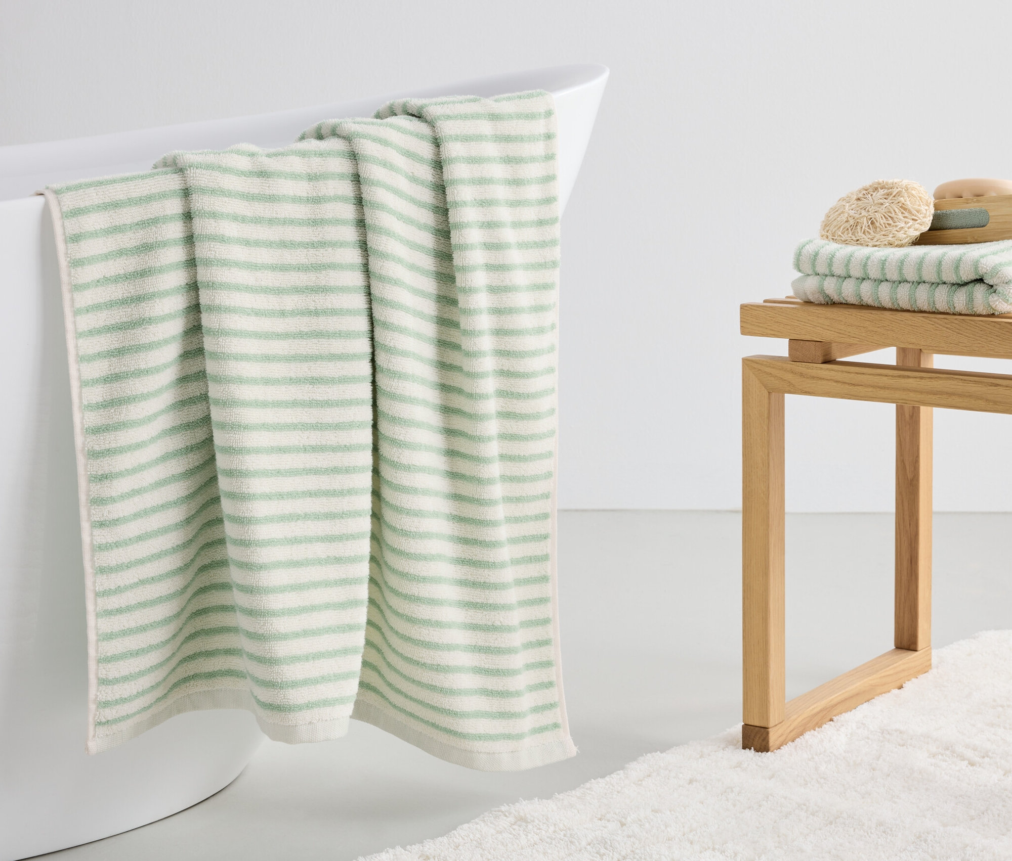 Zelená pruhovaná osuška visí na okraji bílé vany.