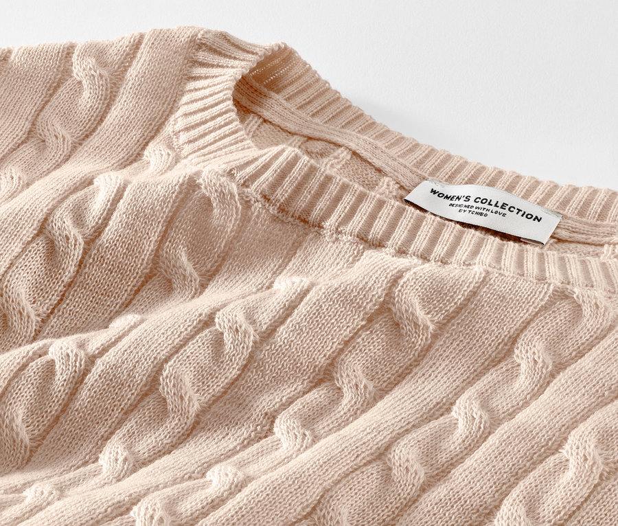 Detail krémového svetru s copánkovým vzorem.