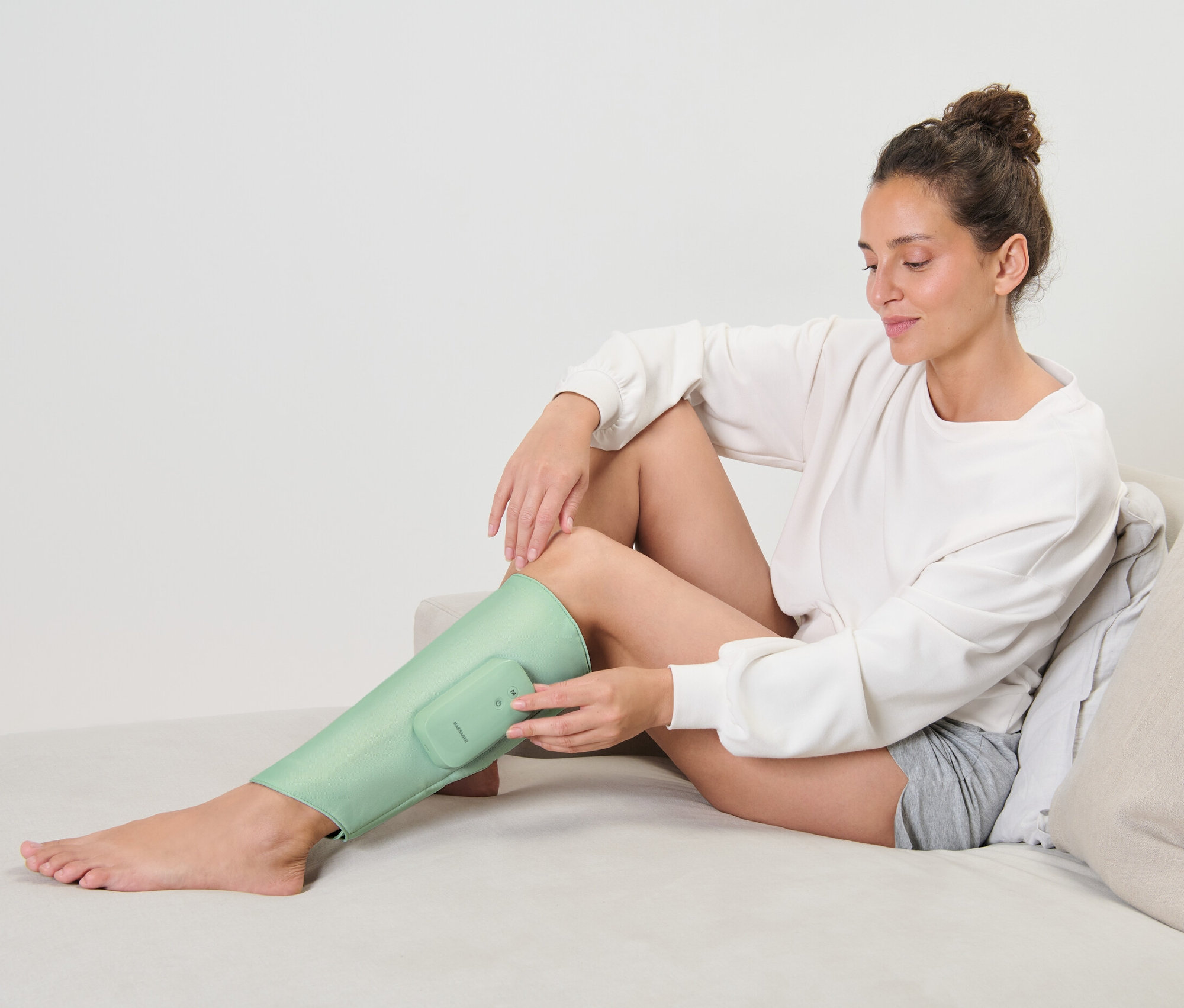 Žena sedí na gauči a používá nabíjecí masážní manžetu na nohu.