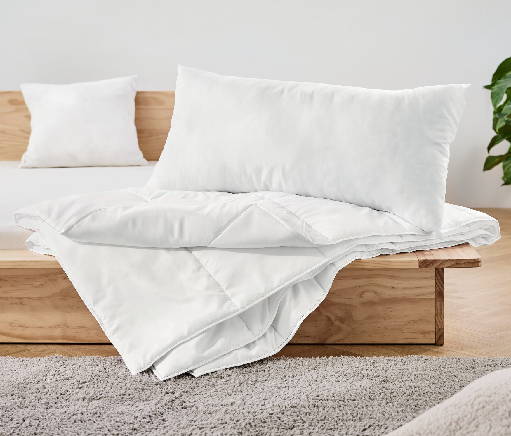 Na dřevěné posteli leží bílá dvoudílná souprava lůžkovin.