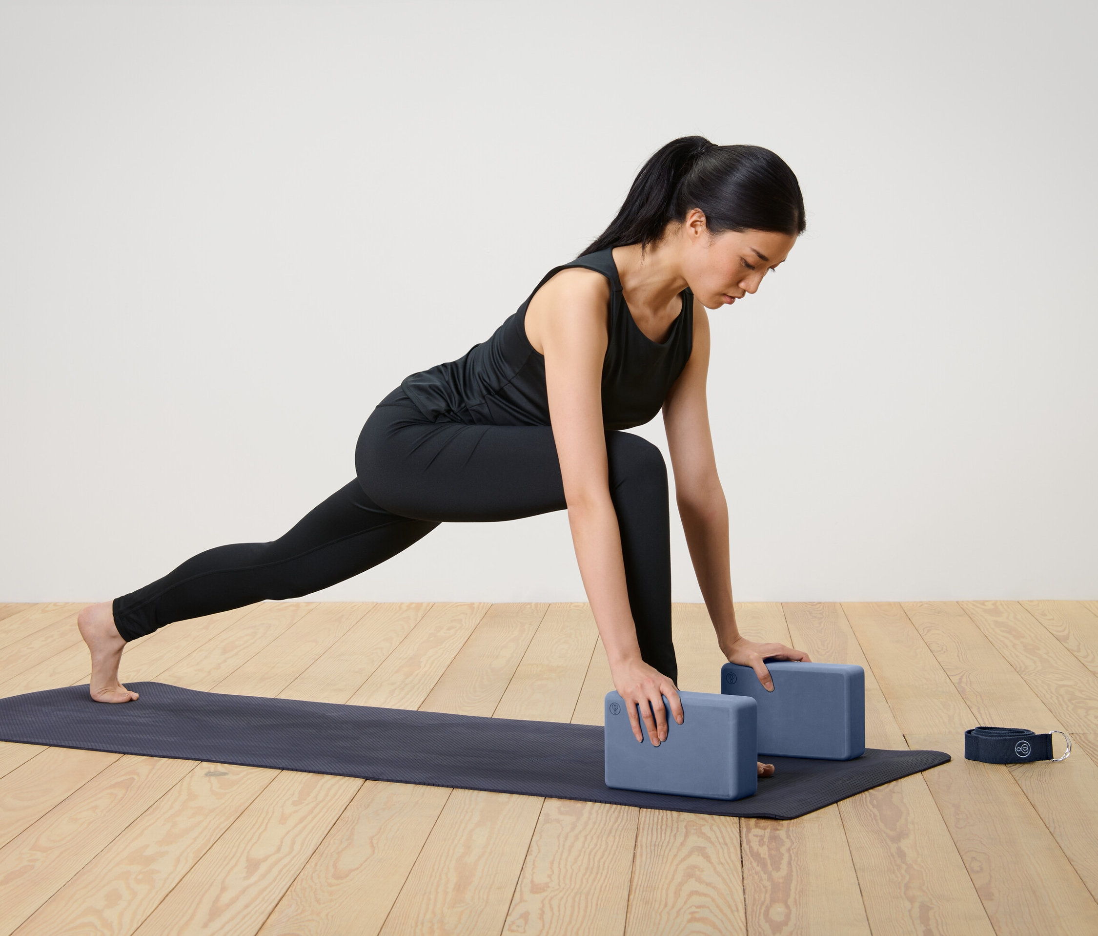 Žena cvičí pozici ještěrky s pomocí sady pomůcek na jógu, která obsahuje dva bloky a popruh.