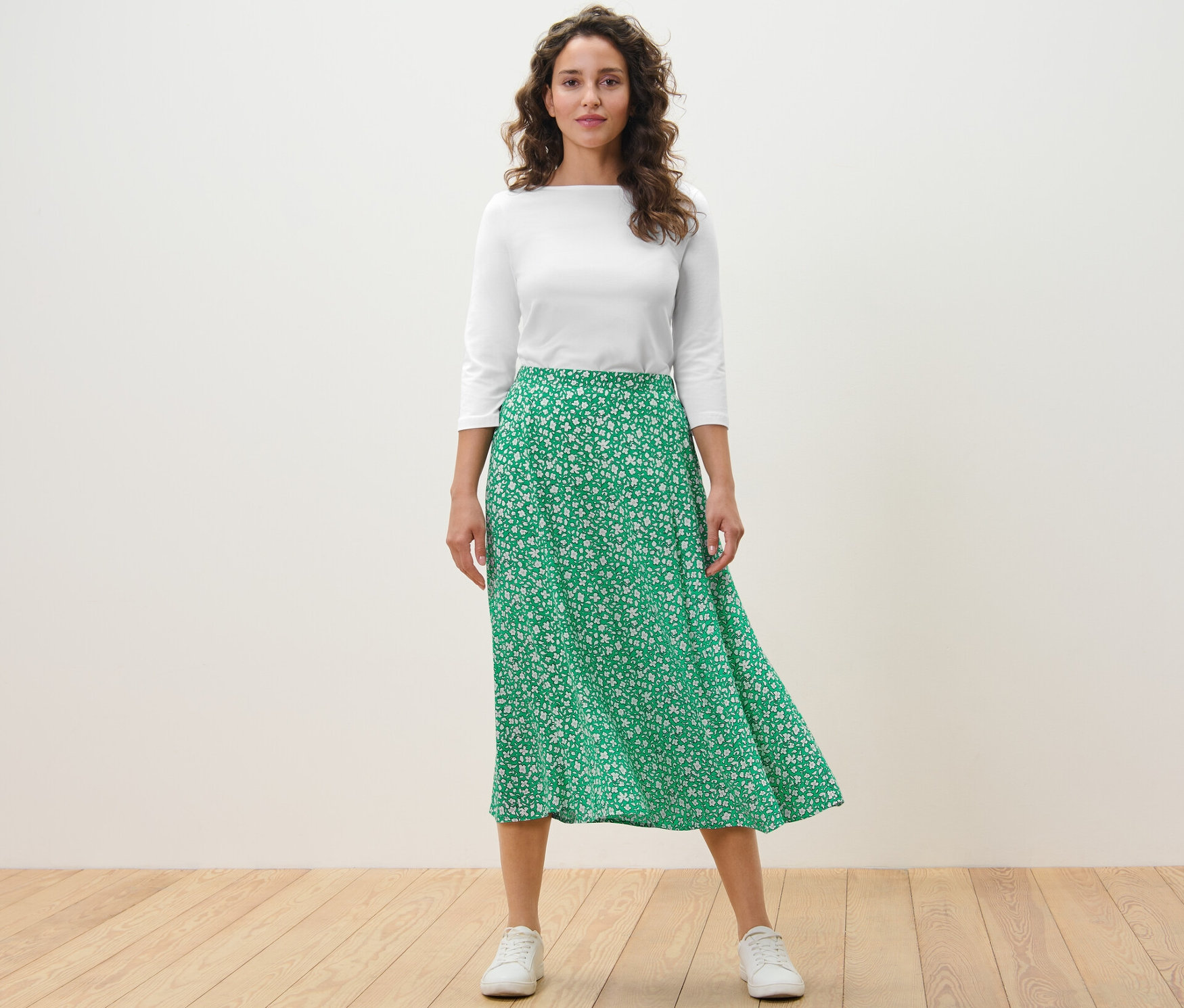 Žena stojí a má na sobě zelenou midi sukni s potiskem.