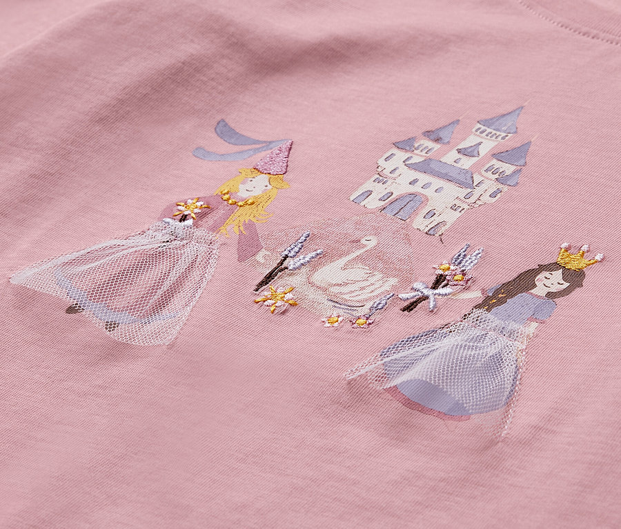 Detail růžového trička s potiskem dvou princezen, labutě a hradu.