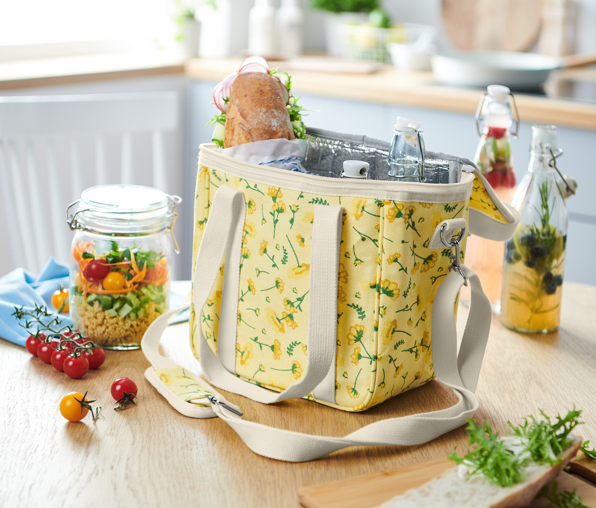 Chladicí taška s květinovým vzorem stojí na stole vedle sklenice se salátem.