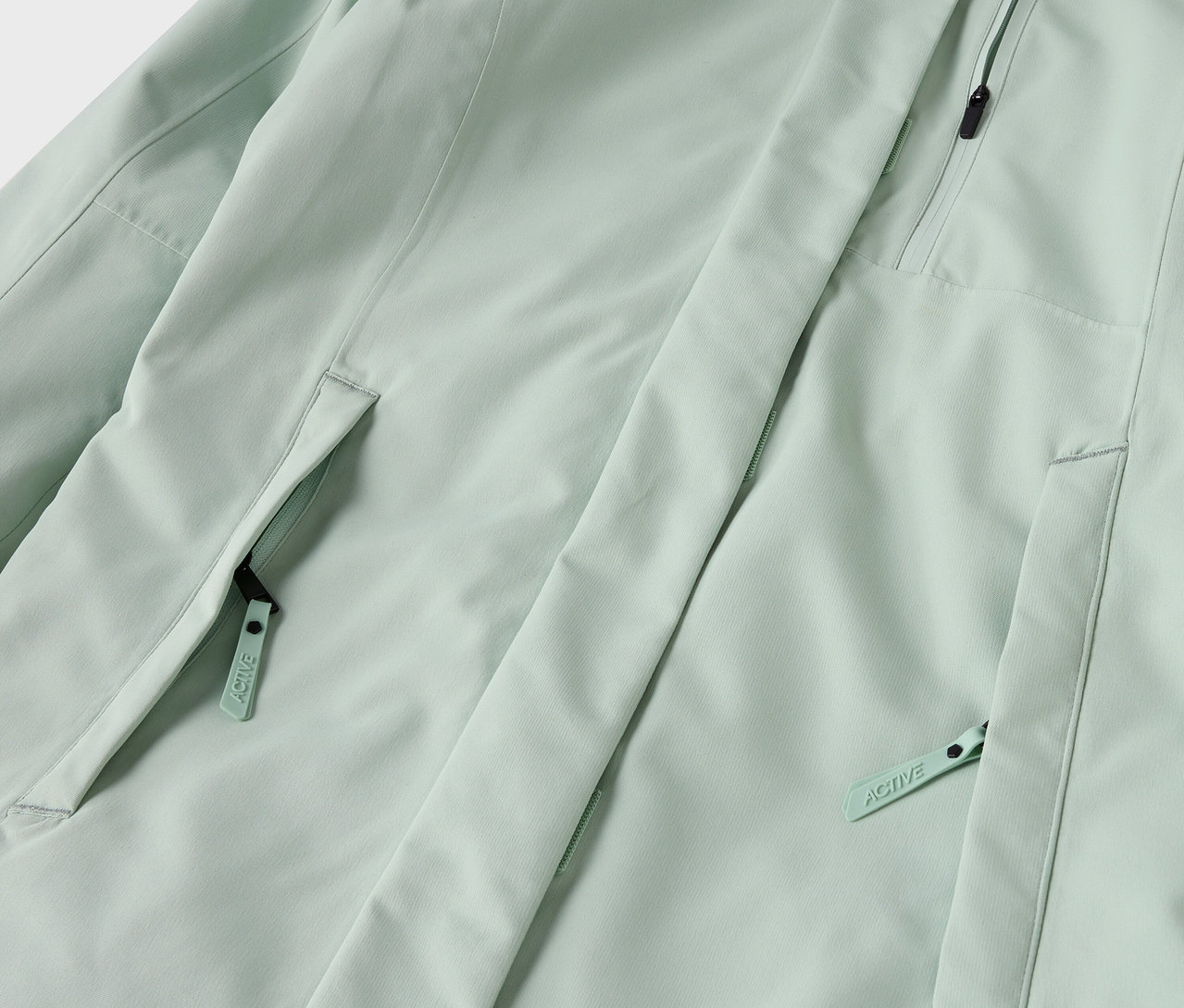 Detail světle zelené bundy s kapsami na zip.