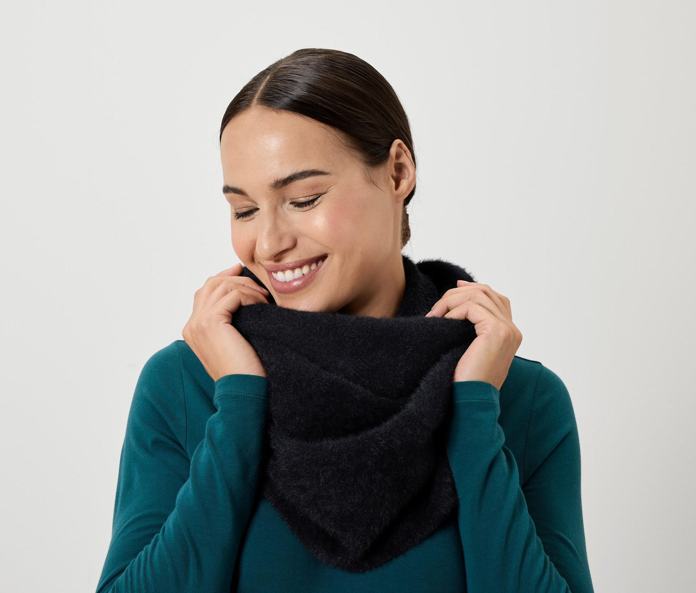 Usmívající se žena se dívá dolů a rukama si přidržuje černý šátek kolem krku.