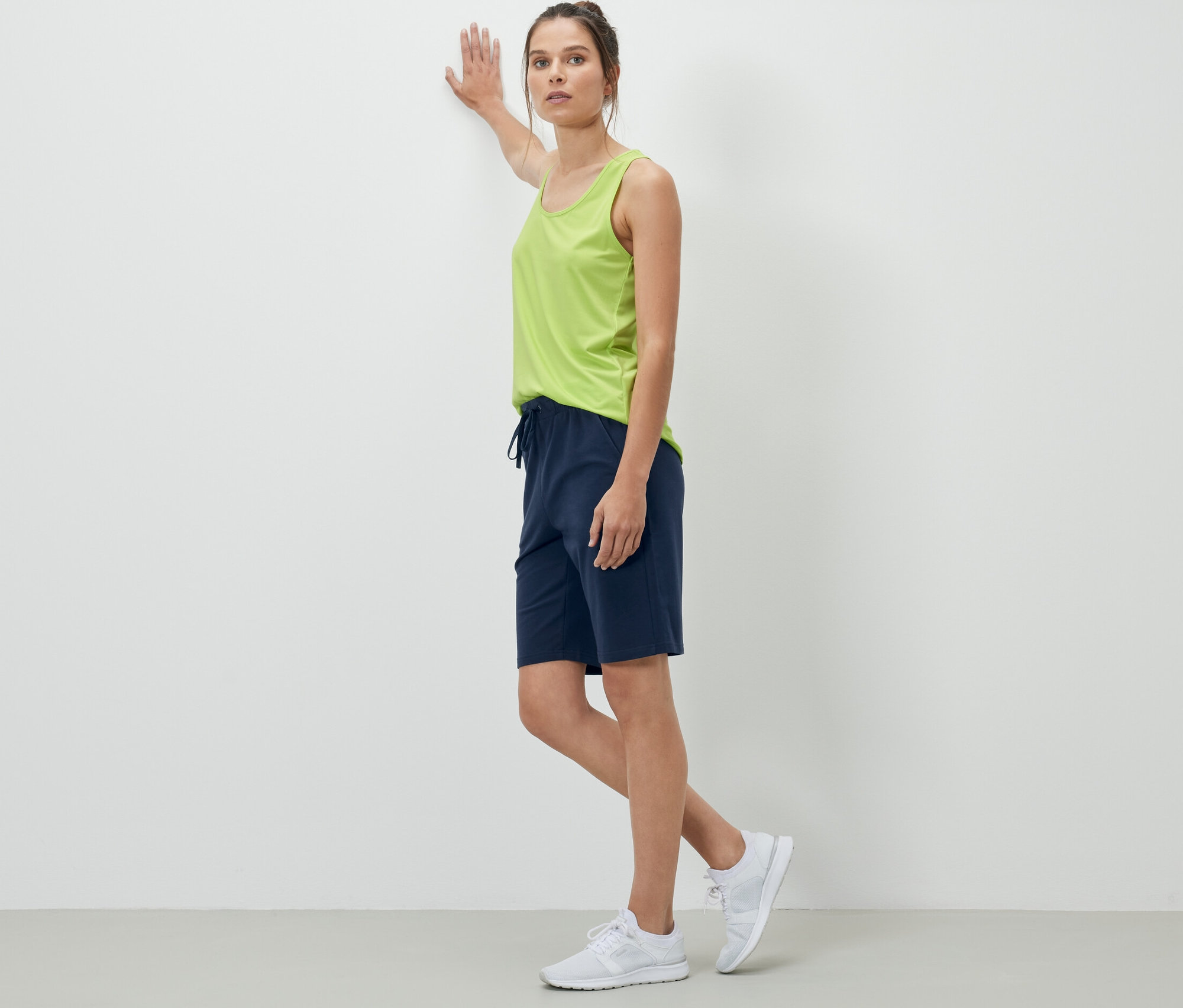 Žena opírající se o zeď má na sobě tmavě modré teplákové šortky.