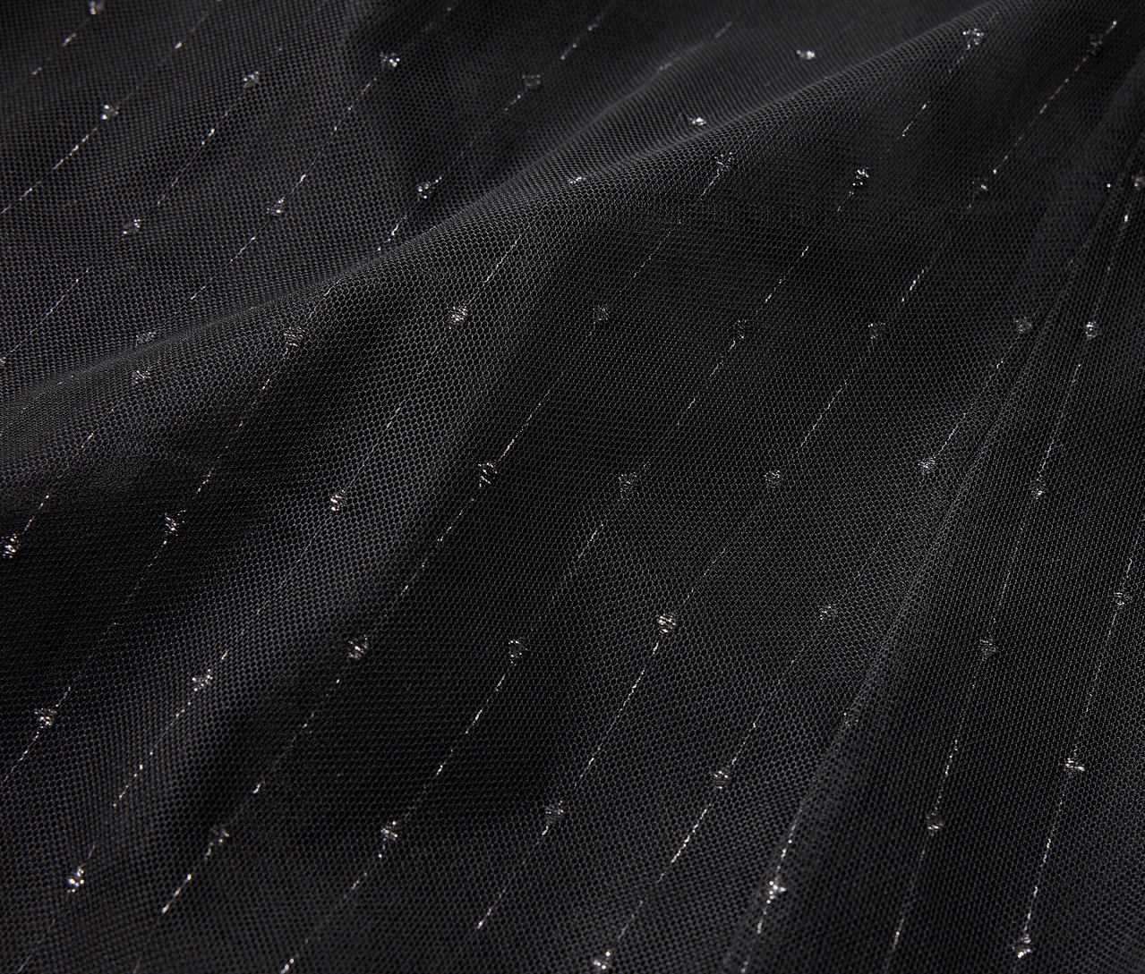 Detailní záběr černé látky s diagonálními stříbrnými proužky a tečkami.