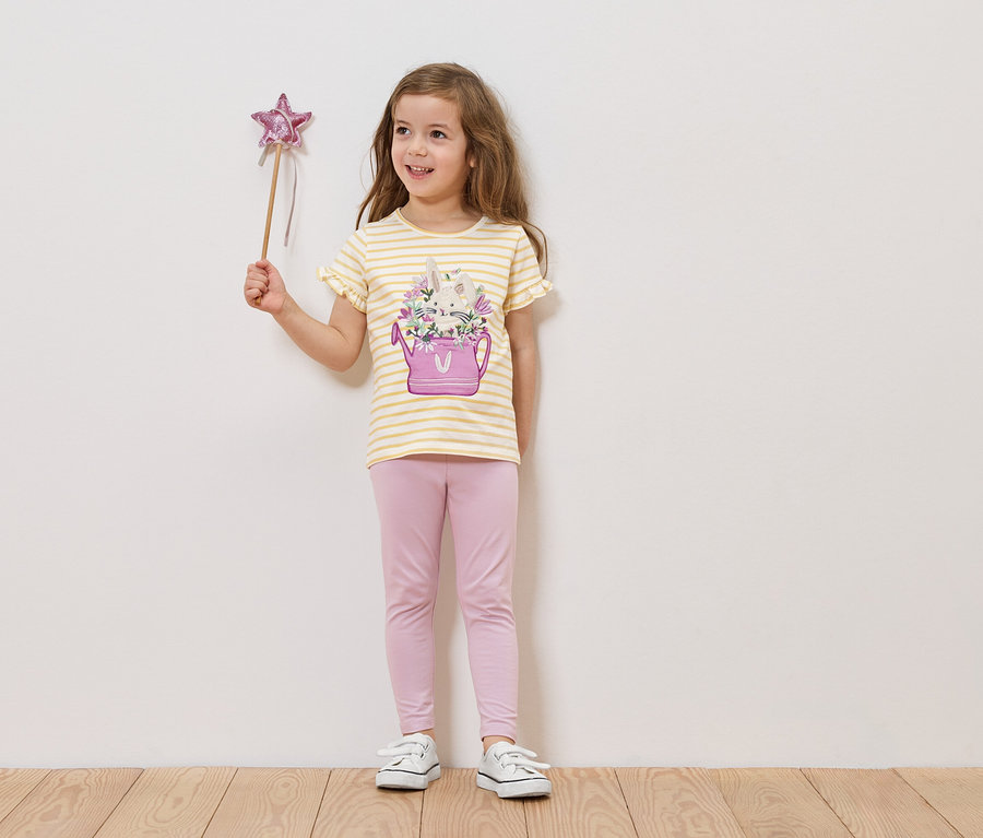 Dívka drží hůlku s hvězdou, má na sobě tričko s obrázkem konve s květinami a růžové legíny.