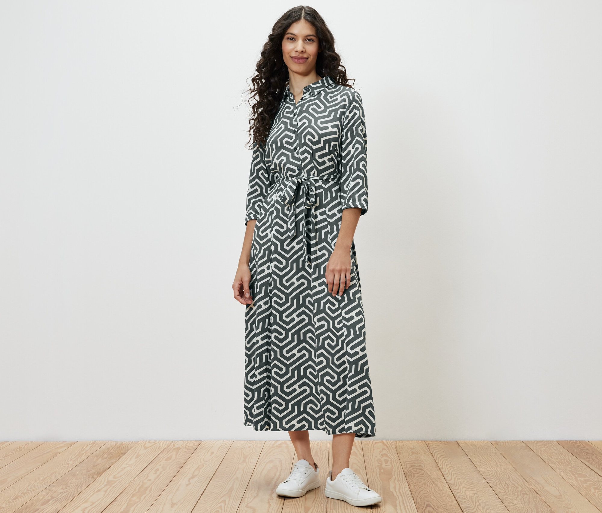 Žena stojí a má na sobě košilové šaty s potiskem.