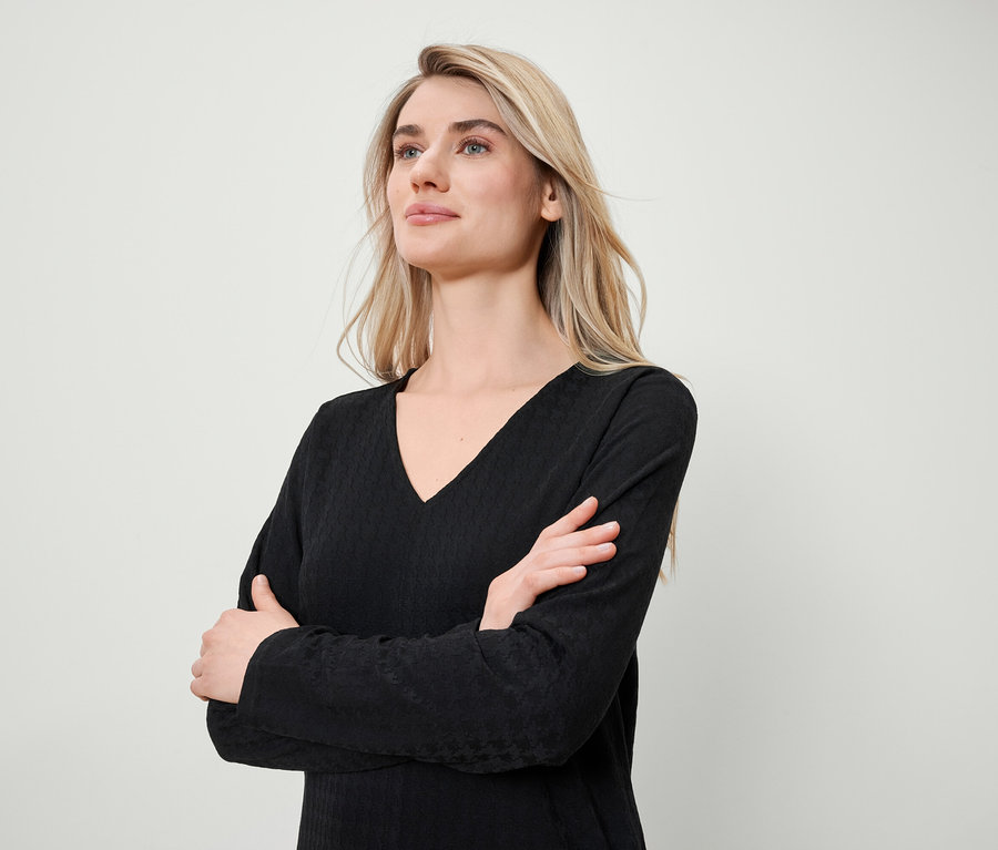 Blondýna se zkříženýma rukama má na sobě černé tričko s dlouhým rukávem a výstřihem do V.