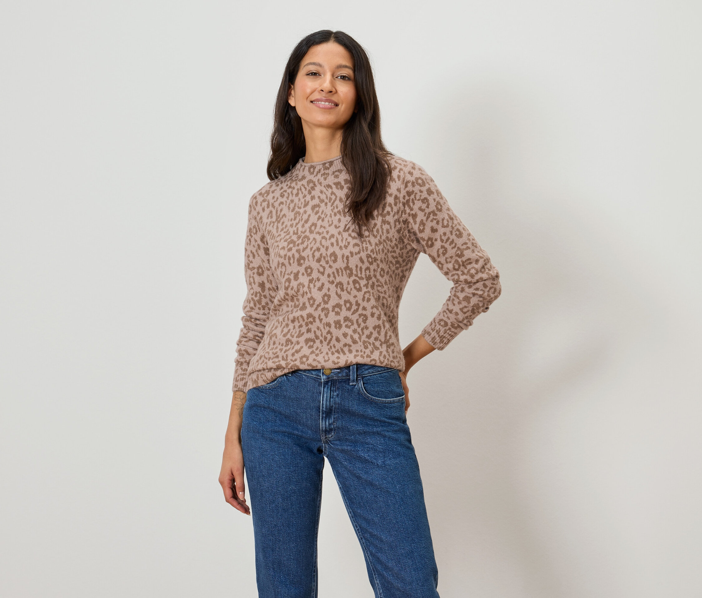 Žena má na sobě světle hnědý svetr s leopardím vzorem a modré džíny.