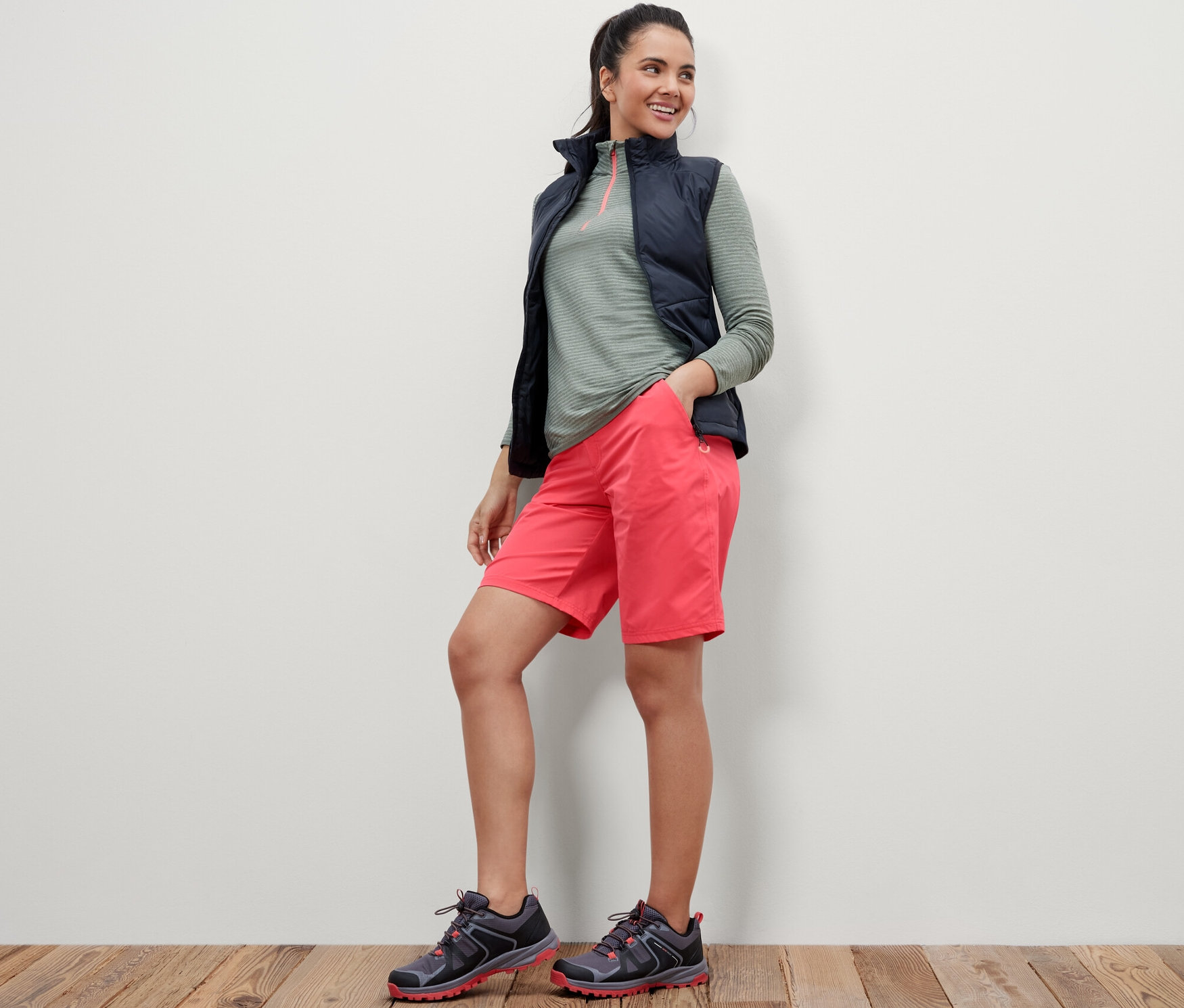 Žena stojí a má ruce v kapsách růžových softshellových funkčních šortek.
