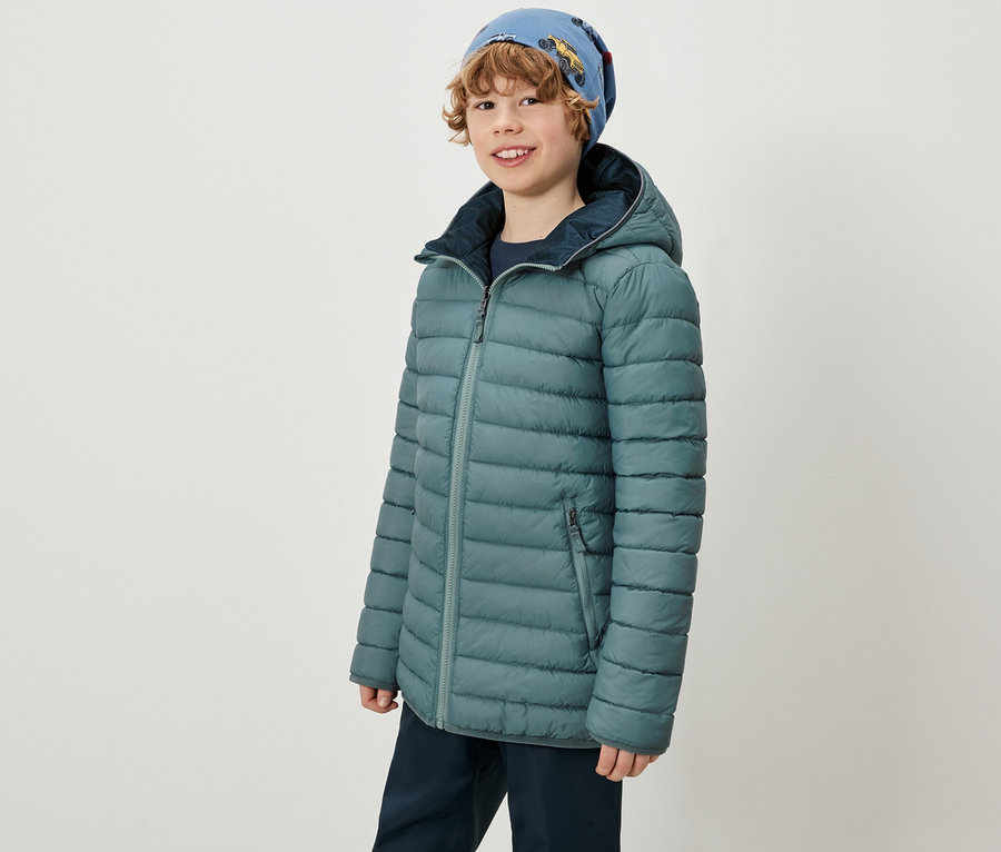 Chlapec má na sobě 2-in-1-Kinder-Softshell-und-Steppjacke a modrou čepici.