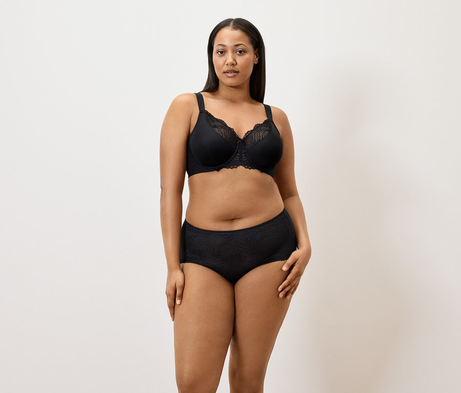 Žena má na sobě černou zmenšující podprsenku a černé kalhotky (5 ks) na bílém pozadí.