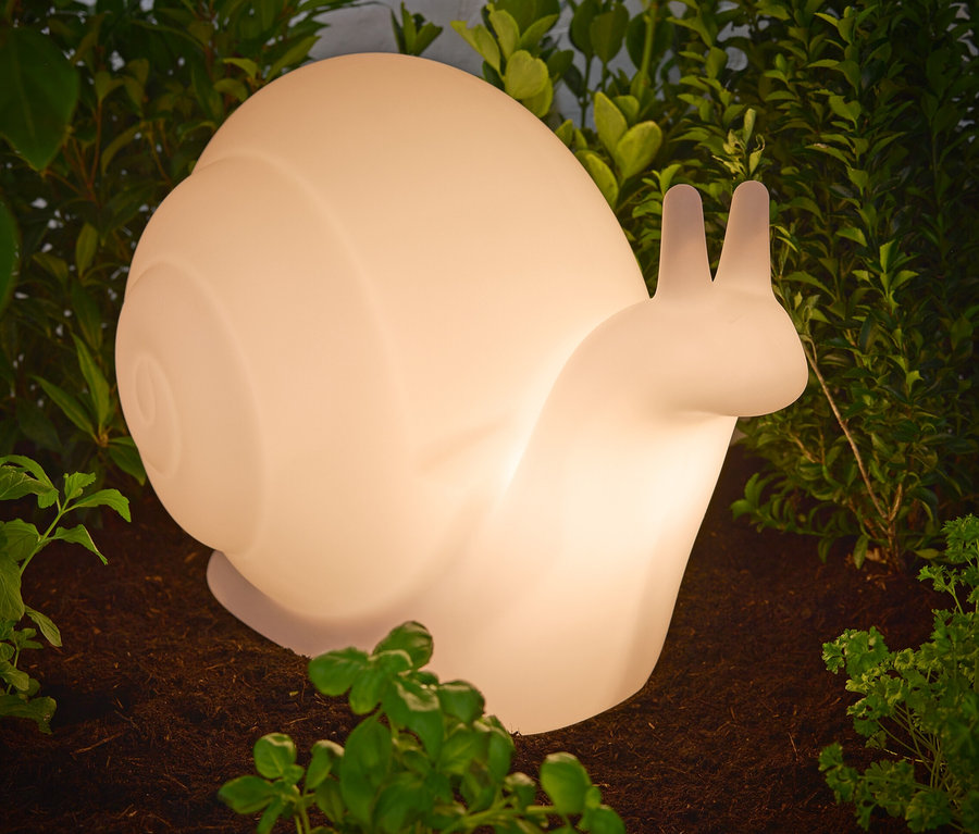 Snímek solárního svítidla Premium „Šnek“ umístěného na zemi mezi rostlinami.
