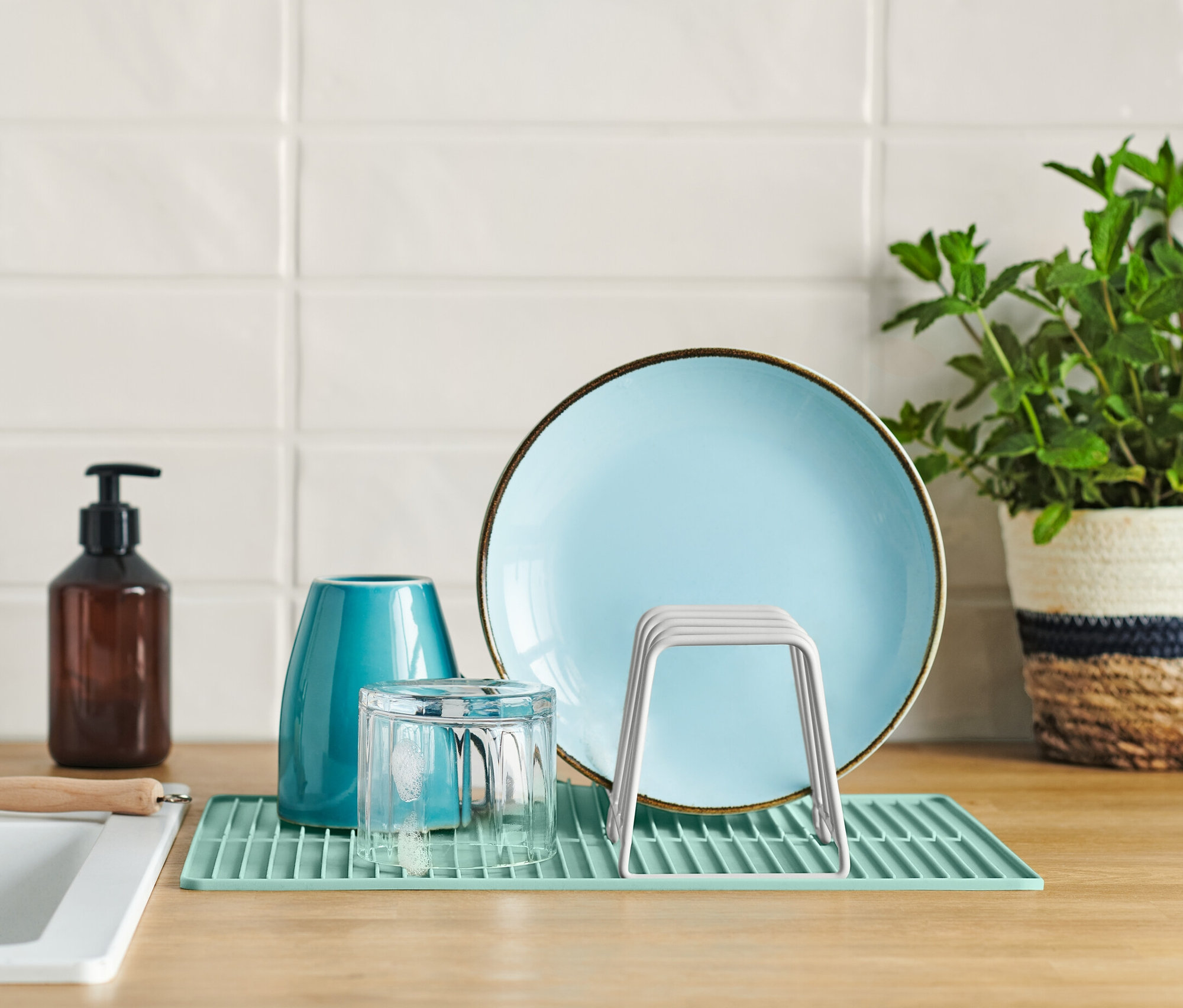 Modrý talíř, sklenice a odkapávač na nádobí se silikonovou podložkou na lince u dřezu.