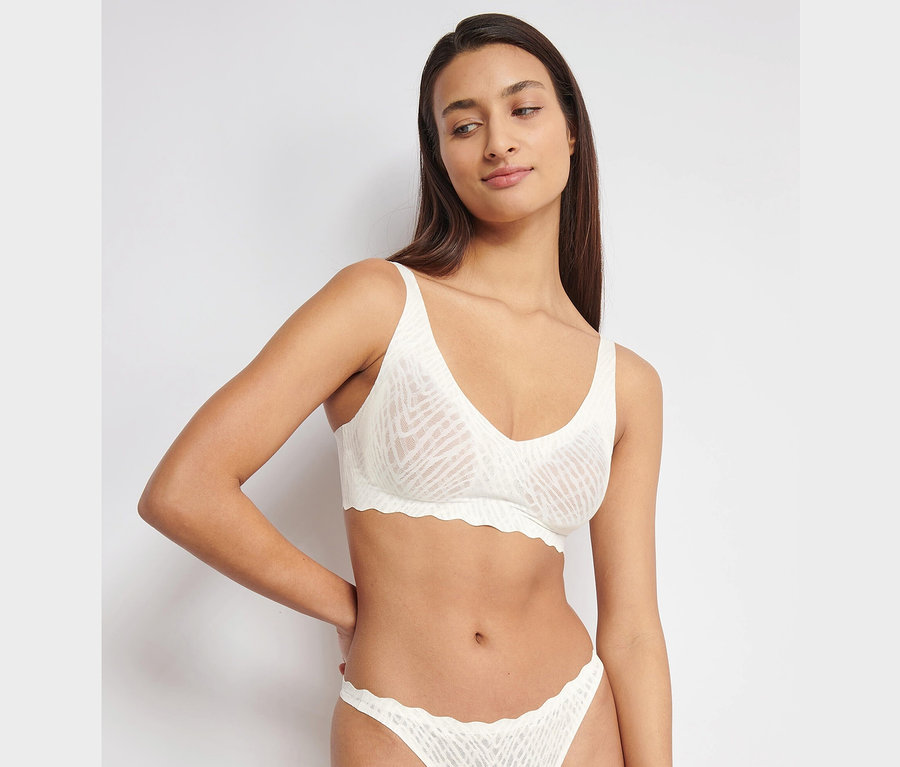 Žena má na sobě měkkou podprsenku sloggi ZERO Feel Bliss Soft Bra v hedvábně bílé barvě a odpovídající kalhotky.
