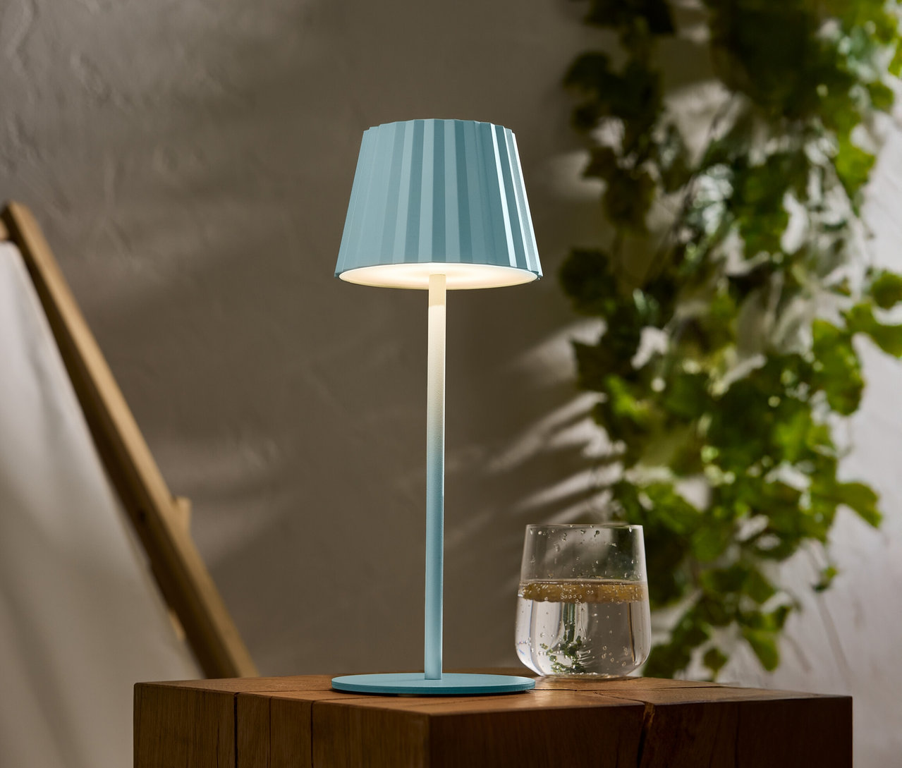 Modrá pruhovaná lampa stojí na dřevěném stole vedle sklenice vody.