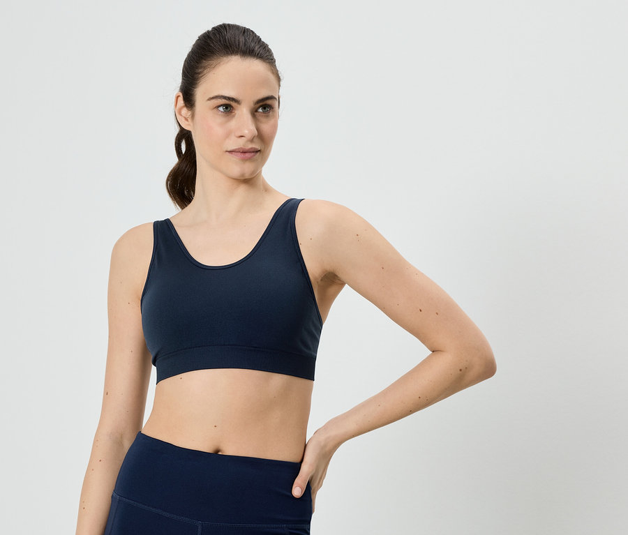 Žena s culíkem v tmavě modré sportovní podprsence a legínách, která si dává ruku na bok.