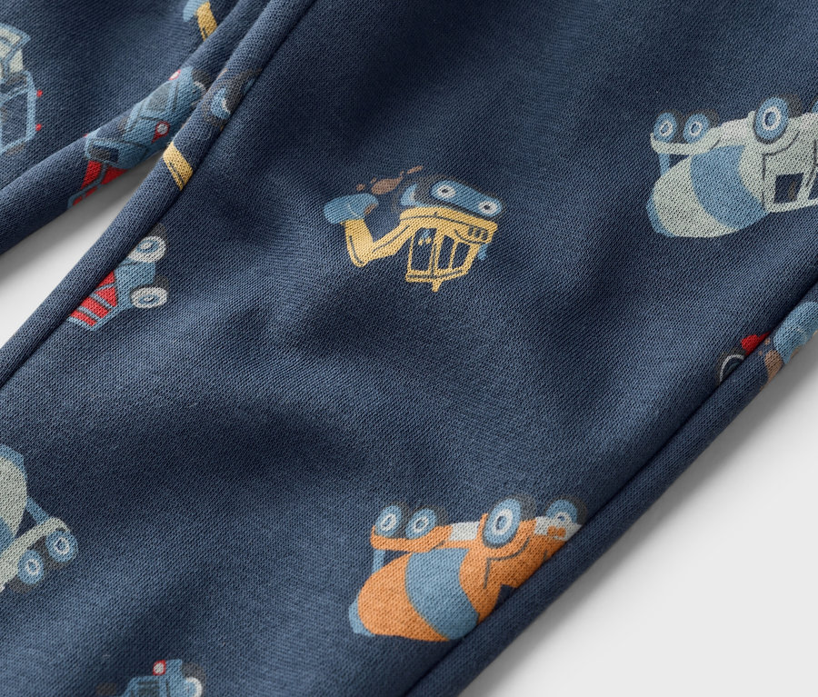 Detailní záběr na tmavě modré kalhoty s celoplošným potiskem stavebních vozidel.