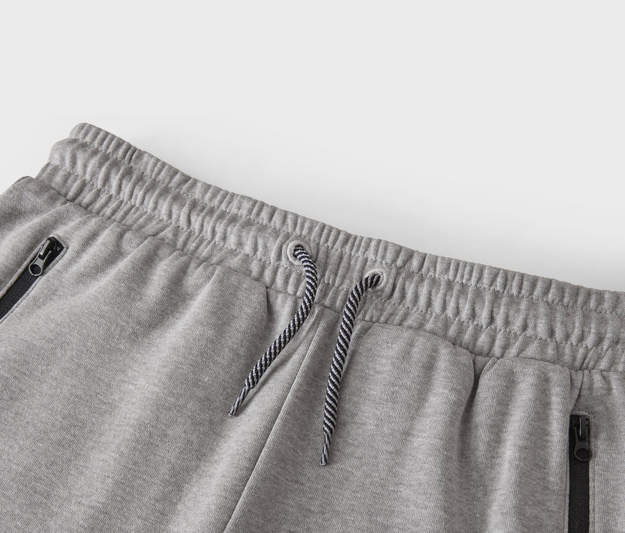 Detailní záběr na pas šedých tepláků se stahovací šňůrkou a kapsami na zip.