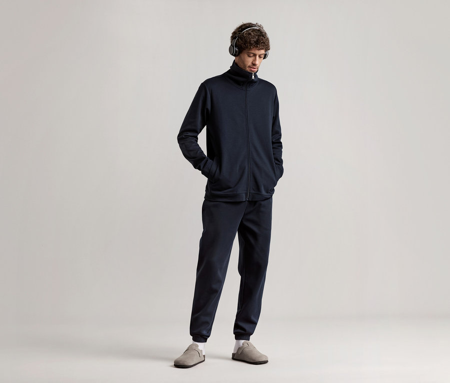 Muž se sluchátky na uších v tmavě modré domácí soupravě.