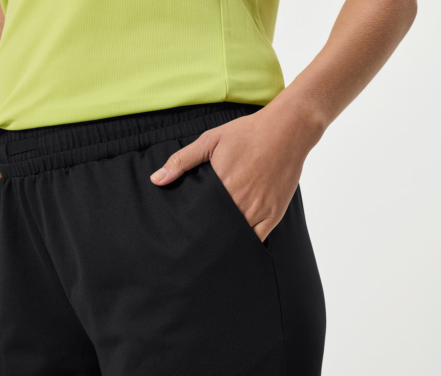 Detail osoby v černých teplácích a žlutém topu, která si dává ruku do kapsy.