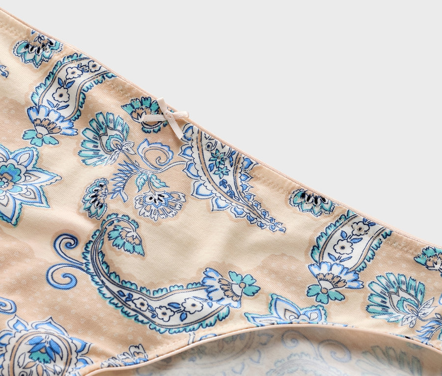 Detailní záběr na béžové kalhotky s modrým paisley vzorem a mašlí.