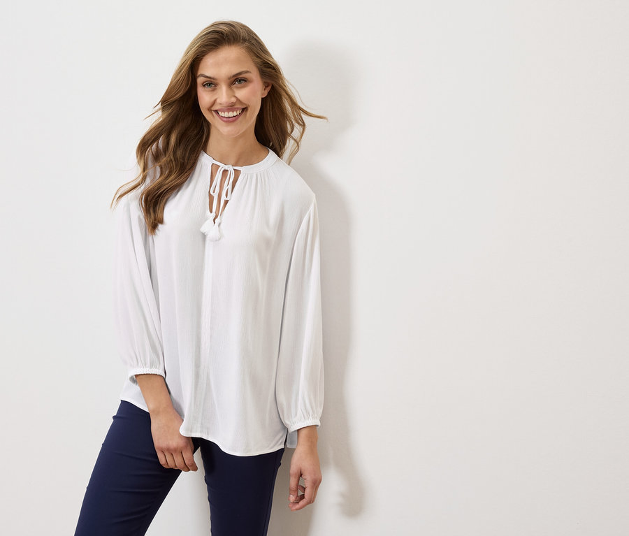 Žena má na sobě bílou blůzu s dlouhými rukávy a tmavě modré kalhoty.