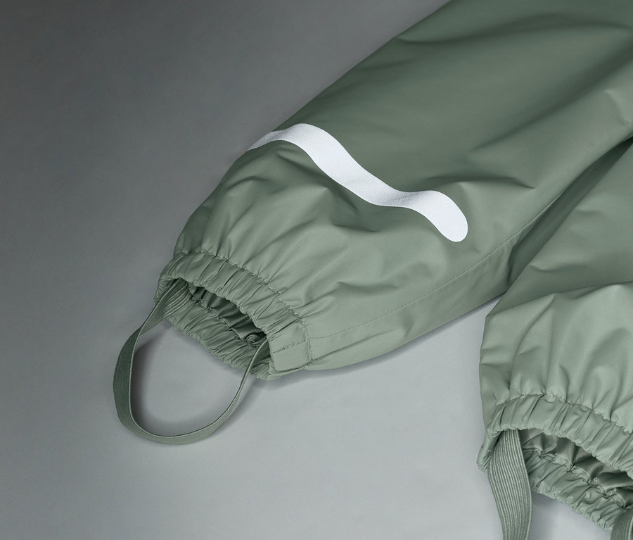 Detailní záběr na světle zelené nepromokavé kalhoty s bílým logem a elastickými manžetami.