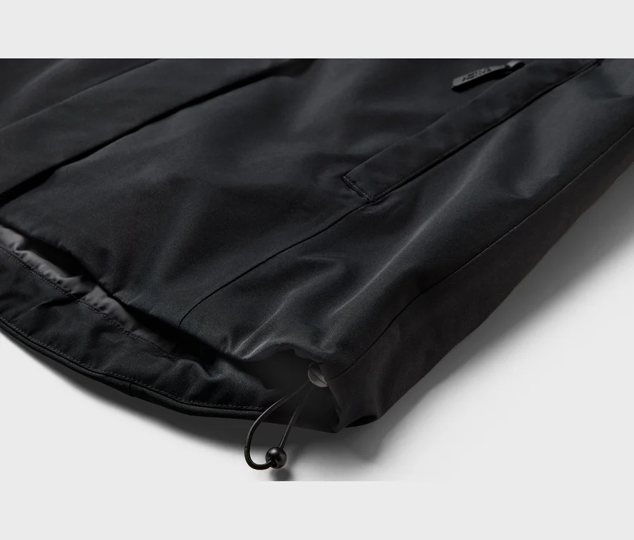 Detail lemu černého oděvu s tunýlkem na stahování s černými zarážkami a kapsou na zip.