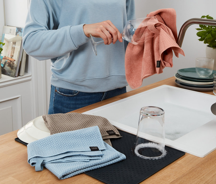 Žena utírá sklenici růžovou utěrkou na nádobí ze sady 3 kusů.