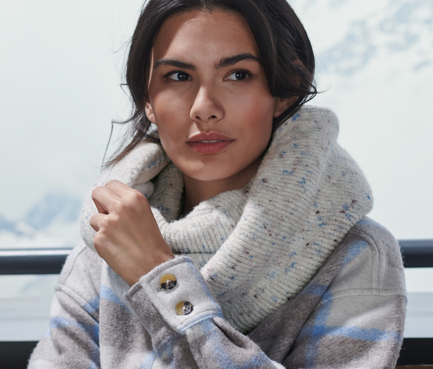 Žena sedí venku a má na sobě pletenou kruhovou šálu.