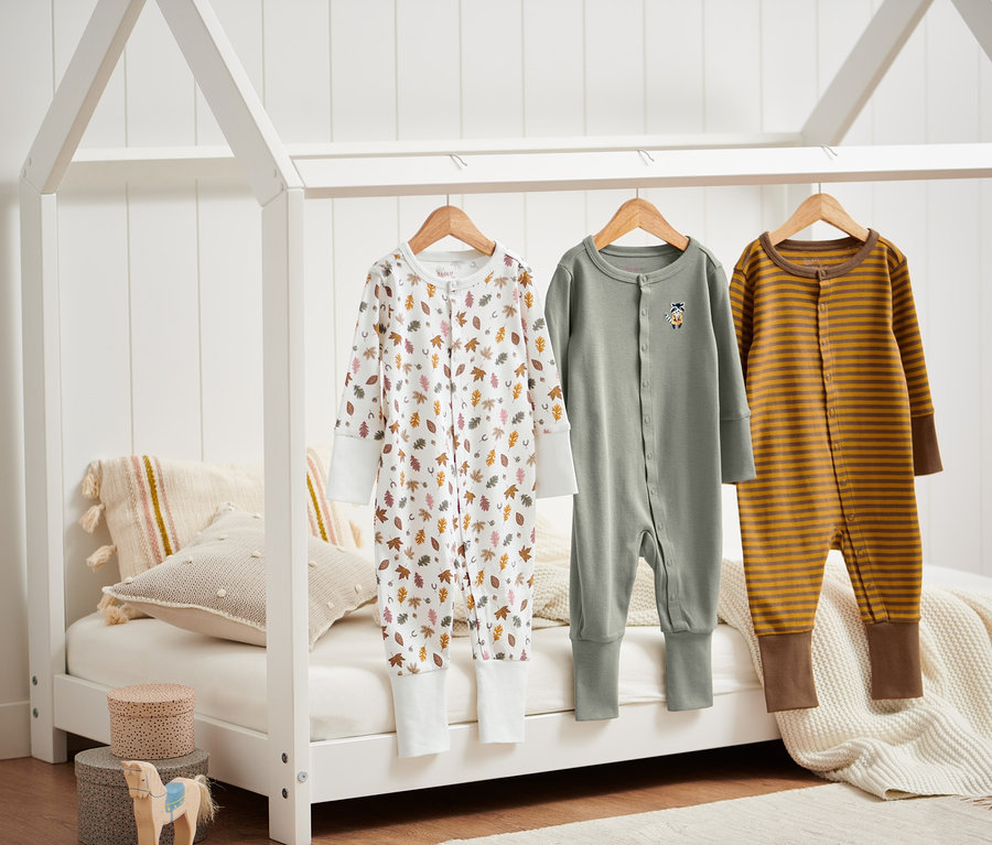 Tři pyžamka visí na rámu postele.