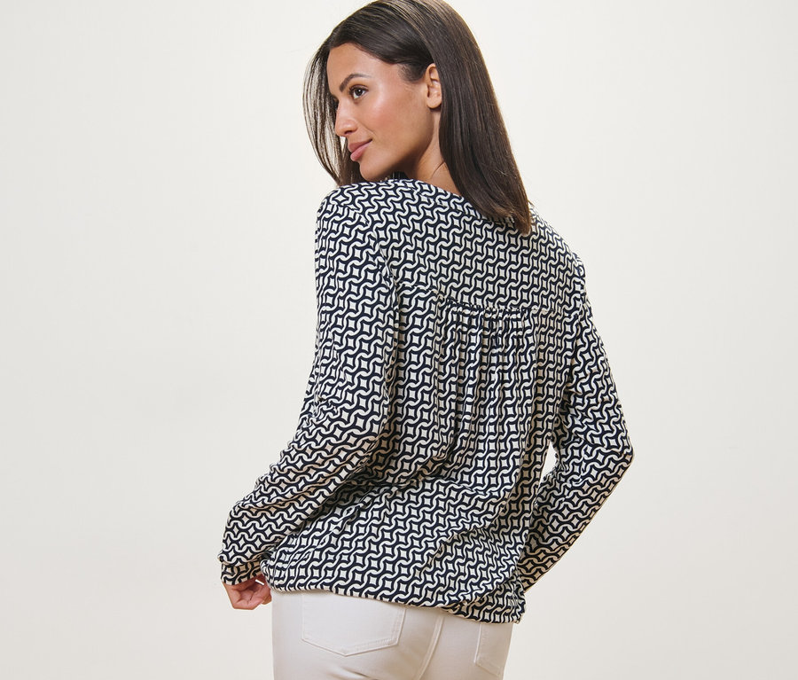 Žena se dívá přes rameno a má na sobě halenkové triko s potiskem, námořnická modrá.