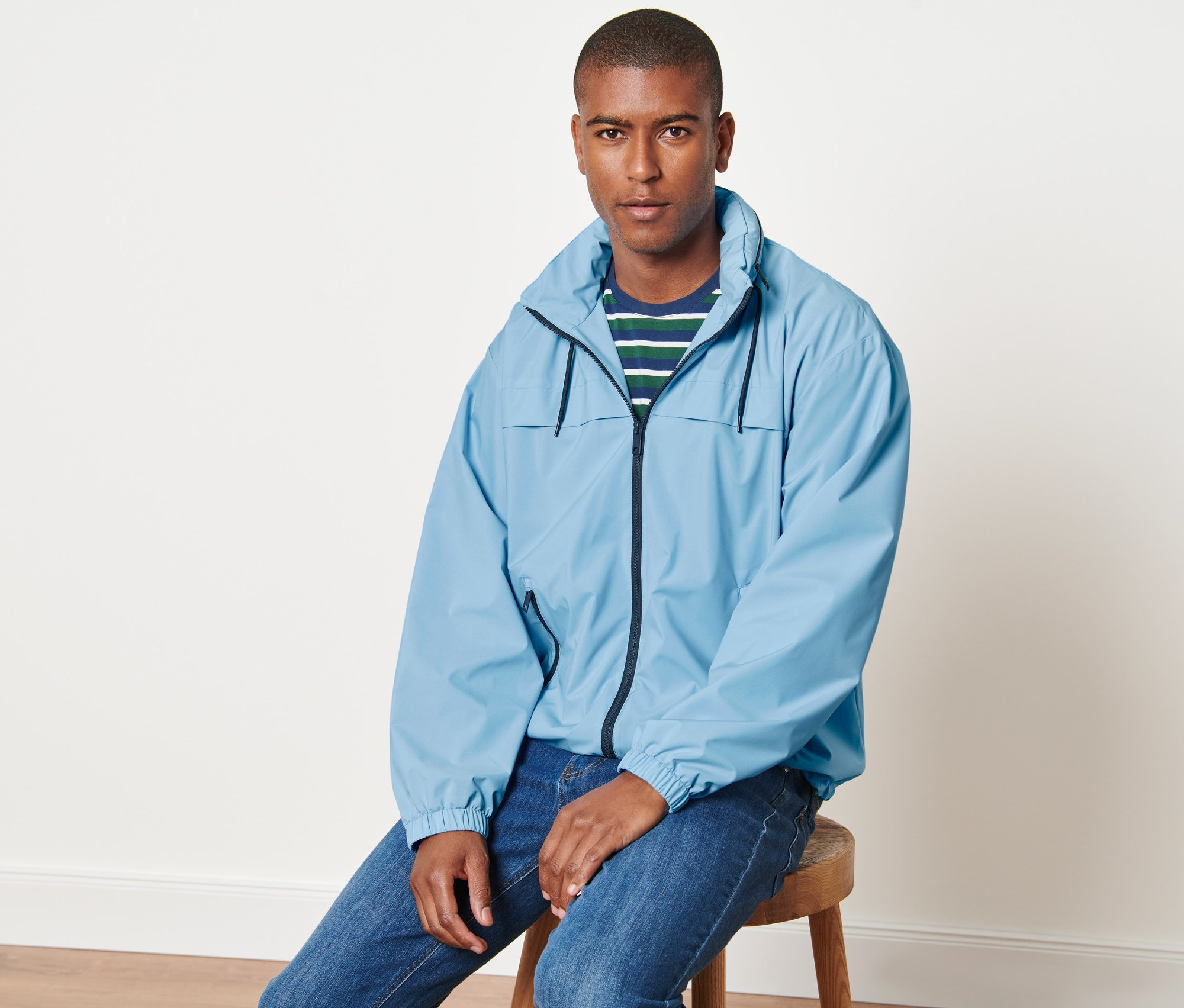 Muž sedí na stoličce a má na sobě světle modrou větrovku.